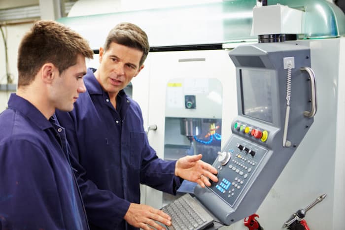 Engineer And Apprentice Using Automated Milling Machine Together